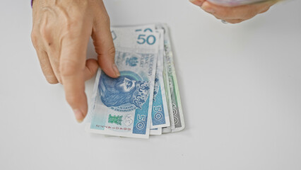 A mature woman counts polish zloty banknotes against a white background, indicating finance management and savings.