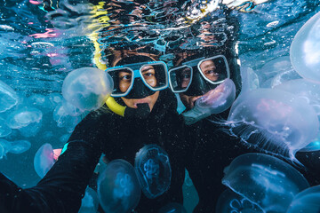 Two people are underwater with jellyfish surrounding them