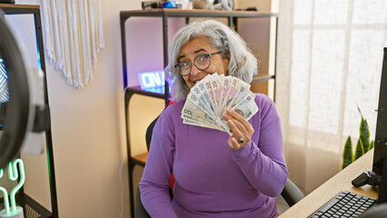 A mature woman in a purple sweater holds polish zloty in a well-lit gaming room, smiling behind the...