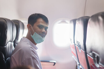 A young man dons a protective face mask while seated inside an airplane, illustrating safe travel...