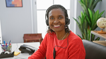 Smiling african woman wearing headset in modern office interior.