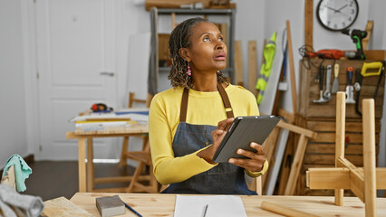 African american woman using a tablet in a carpentry workshop looking focused and entrepreneurial