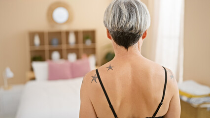 Mature woman with grey hair and tattoos in a cozy bedroom setting, embodying tranquility and...