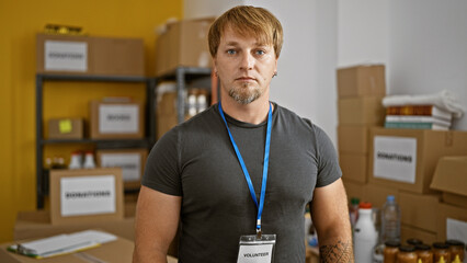 Blond man with beard wearing volunteer id standing confidently in a warehouse with cardboard boxes...
