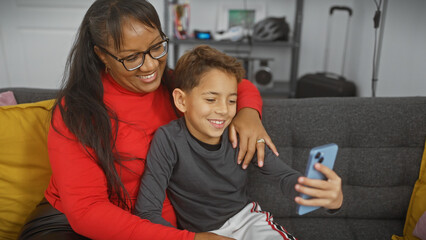 A smiling woman and boy enjoying time together taking a selfie on a couch in a cozy living room.
