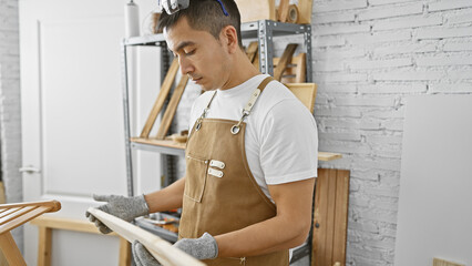 Hispanic man in apron inspecting wood in a carpentry workshop, embodying craftsmanship and skill.