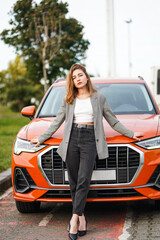 Brooding girl standing in front of her car and looking straight at camera.
