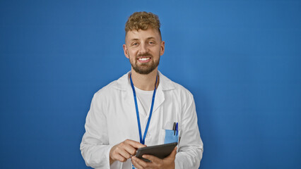 A smiling caucasian man with a beard, wearing a lab coat and holding a tablet, stands against an...
