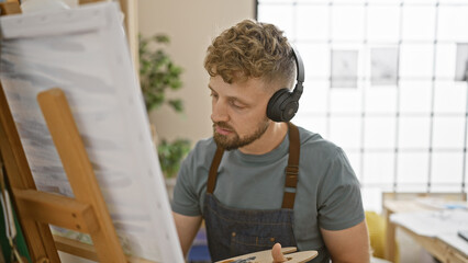 Focused young man with headphones painting on a canvas in a bright art studio