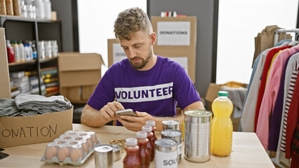 Young man volunteer sorting donations in warehouse using smartphone