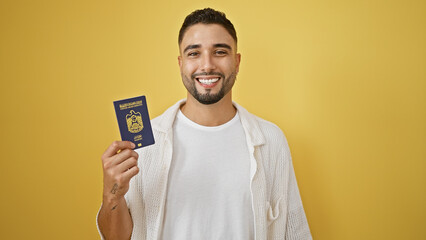 Handsome young man with a beard smiling and holding a uae passport against a yellow isolated...