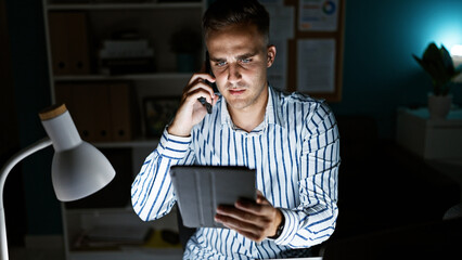 Handsome man using tablet and phone in a modern office at night, conveying business, technology, and multitasking.