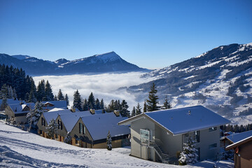 Sattel, Swiss Alps. A picturesque winter scene: houses nestled in a snowy valley, cozy and adorned in white. Majestic mountains, clear sky, and tranquil clouds.
