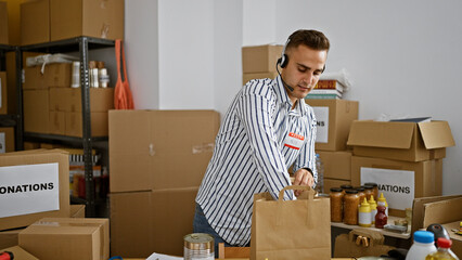 A young man wearing a headset works efficiently in a donation center, surrounded by labeled boxes...