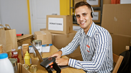 Handsome young man in a striped shirt and headset working at a computer in a warehouse with boxes