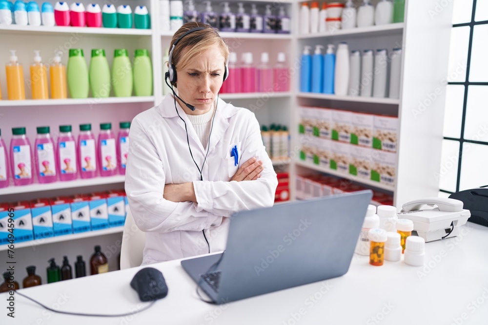 Canvas Prints Young caucasian woman working at pharmacy drugstore using laptop skeptic and nervous, disapproving expression on face with crossed arms. negative person.