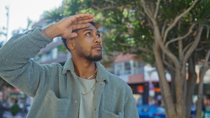 African man shading eyes with hand on a sunlit urban street outdoors © Krakenimages.com