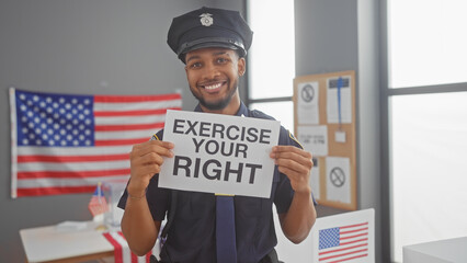Smiling african american policeman holding a 'exercise your right' sign with us flag backdrop in a...
