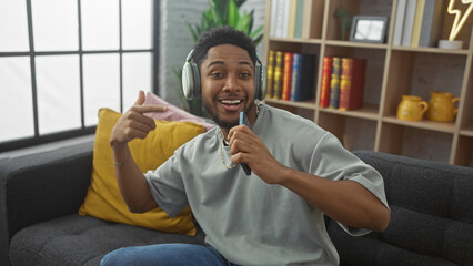 Happy african american man using smartphone as microphone in cozy living room interior.