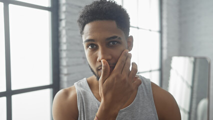 A thoughtful african american man poses in a modern home's living room, exuding casual sophistication.