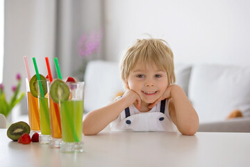 Cute toddler child, blond boy, drinking freshly made fruit juice at home