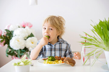 Little toddler child, blond boy, eating boiled vegetables, broccoli, potatoes and carrots with fried chicken meat at home