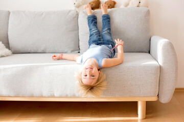 Toddler child, hanging upside down from a couch at home, smiling