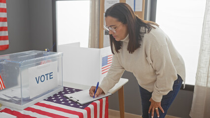 Hispanic woman voting at a polling station with us flags, showcasing democracy and citizenship in a civic duty setting.