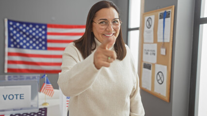 Hispanic woman pointing indoors at a usa electoral college with american flag, smiling and...
