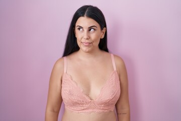 Young hispanic woman wearing pink bra smiling looking to the side and staring away thinking.