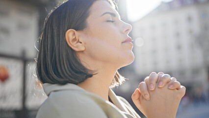 Young beautiful hispanic woman praying with closed eyes in the streets of Vienna