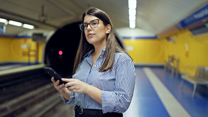 Young beautiful hispanic woman waiting for the subway using smartphone in subway station of Madrid