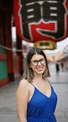 Beautiful hispanic woman donning glasses, flashing a cheerful smile at the senso-ji temple, immersed in japanese tradition, joyful latin adult exploring the rich culture of tokyo