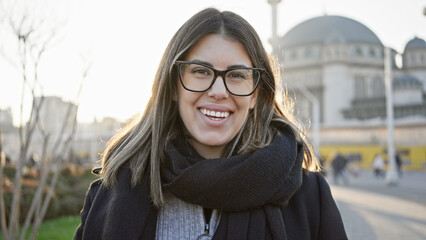 Obraz premium Smiling woman wearing glasses with taksim mosque backdrop in turkey during golden hour