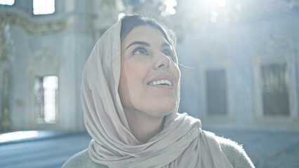 Young adult woman wearing a hijab looking up inside an ornate istanbul mosque, conveying a sense of...
