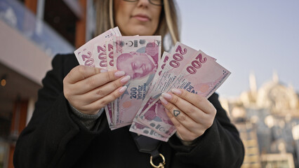 A young adult woman holds turkish lira with a backdrop of istanbul, expressing travel, city life,...
