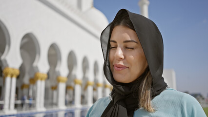 A serene young woman enjoys the peaceful ambiance of an islamic mosque in abu dhabi, uae.