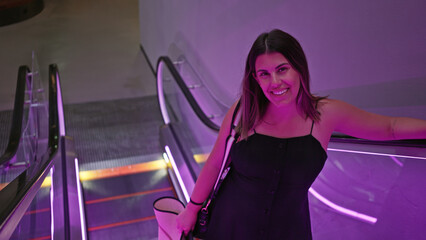 Smiling woman standing on an escalator with neon lights in a modern urban environment.
