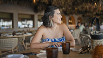 Young hispanic woman smiling happy sitting on the table at the restaurant