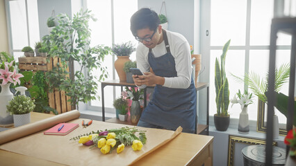 Young asian man using smartphone in a vibrant indoor flower shop surrounded by various plants and...