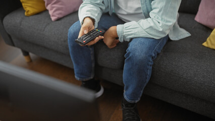 A casual man lounging on a sofa at home holding a remote control, embodying relaxation and domestic...
