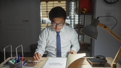 A concentrated asian man in an office analyzing documents under a desk lamp, suggesting a detective...