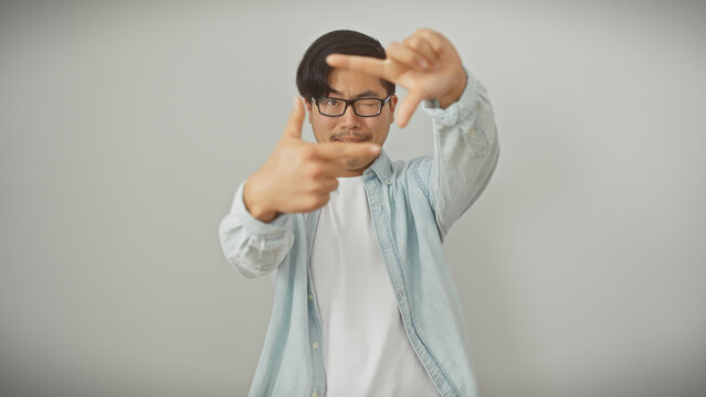 Young asian man makes frame gesture with hands against an isolated white background, depicting creativity or photography concept.