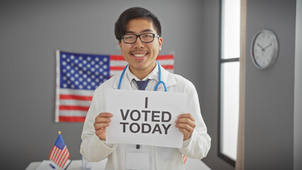 Asian man in lab coat holding 'i voted today' sign with us flag background at polling station.