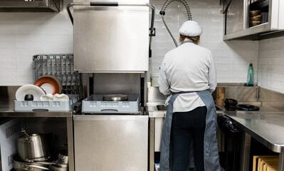 An unrecognizable female cook dressed in a white uniform is cleaning the dishes of a restaurant....