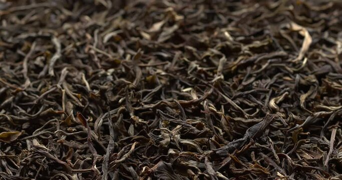 Chinese raw maturing (mao cha) green Pu Erh dried tea leaves as an abstract food background. Table spin. Selective focus.