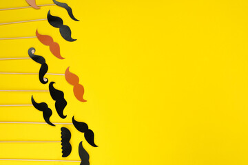 Fake paper mustaches with sticks on yellow background, flat lay. Space for text