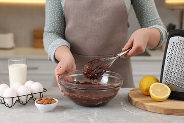 Woman mixing chocolate cream with whisk in bowl at gray marble table indoors, closeup