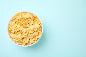 Breakfast cereal. Tasty corn flakes in bowl on light blue table, top view. Space for text
