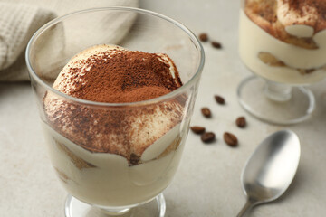 Delicious tiramisu in glass, spoon and scattered coffee beans on light table, closeup